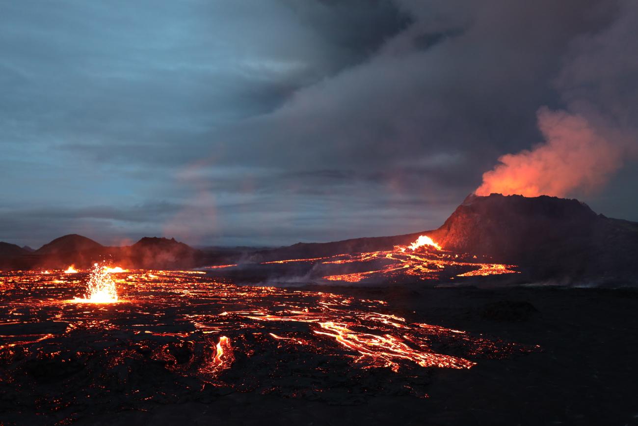 Wide view of lava and smoke erupting from a volcano